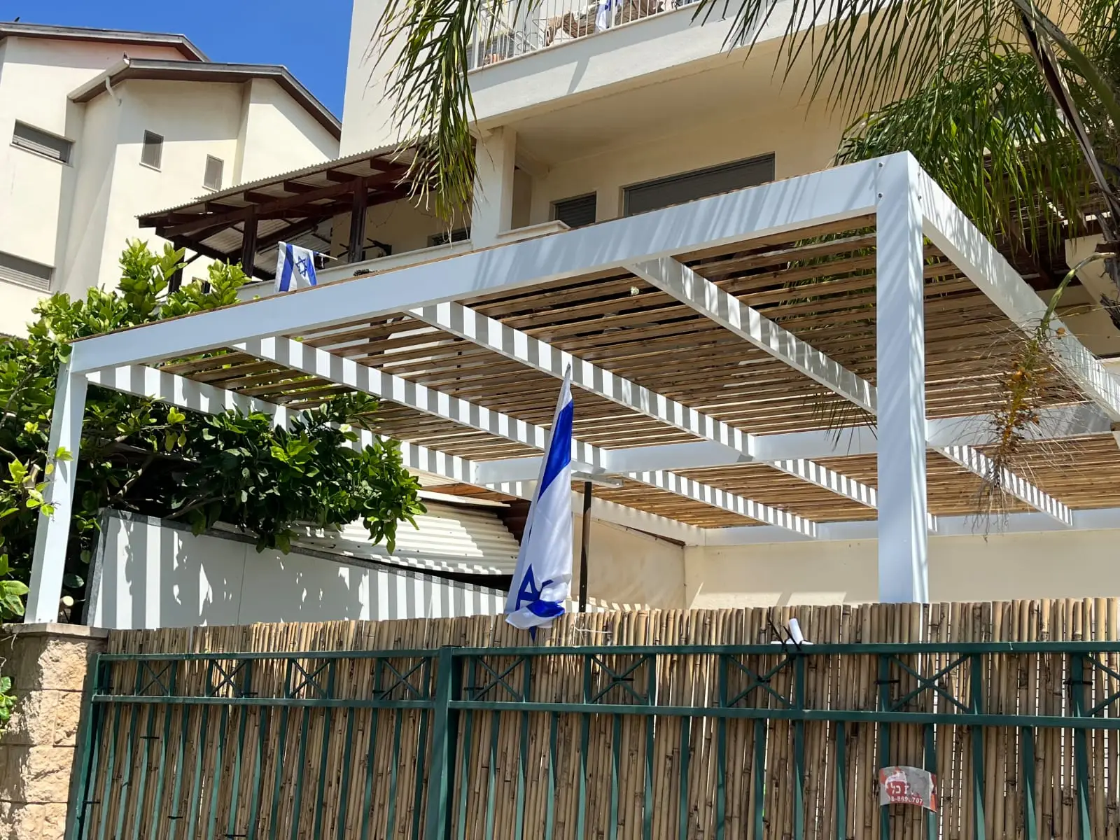 פרגולה לבנה בשילוב עץ בחצר עם דגל ישראל